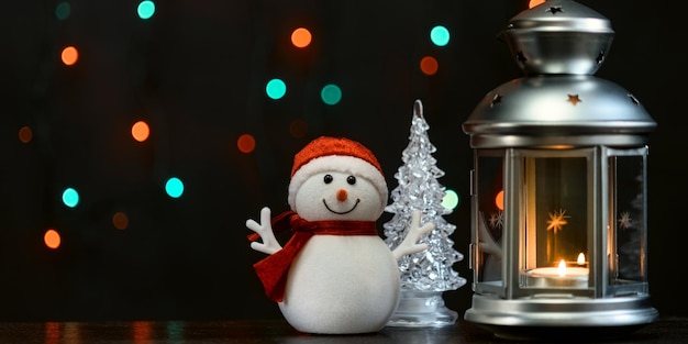 Christmas card a snowman a lantern with candles and blurry lights in the background