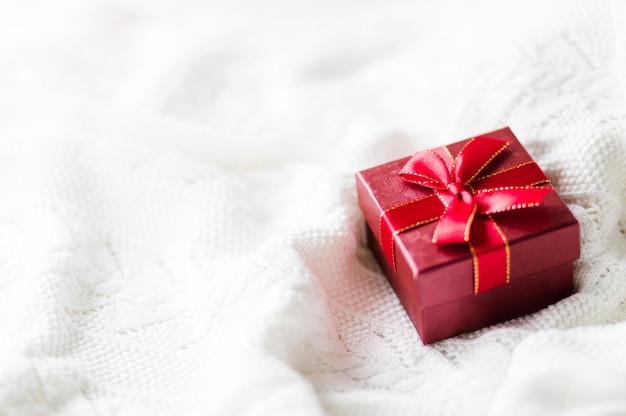 Christmas card with gift box red ribbon on white knitted sweater background. Copyspace. Horizontal photo