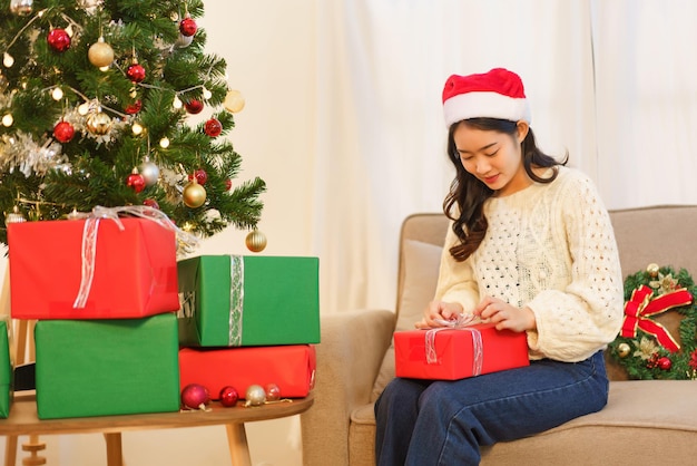 Christmas celebration concept Young asian woman sitting on the couch and opening christmas gift