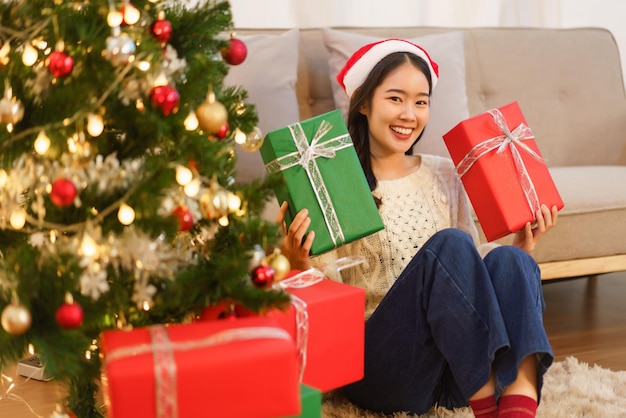 Christmas celebration concept Young asian woman sitting on the floor and holding christmas gifts