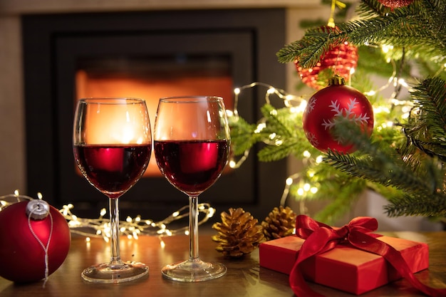 Christmas celebration Red wine glasses Xmas presents and decoration on table fireplace background Xmas celebration