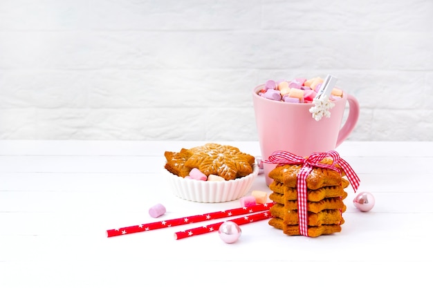 Christmas cocoa with marshmallow in a pink cup and ginger biscuit on a wooden table