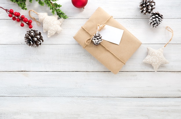 Christmas composition. Christmas gift box, pine cones, fir leaves, holly berry and decoration rustic elements on white wooden background. Creative flat lay, top view design