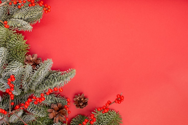 Christmas composition. Christmas red decorations, fir tree branches with bumps on red background. Flat lay, top view, copy space.