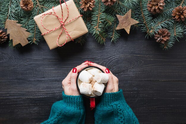 Christmas composition of fir branches, wooden toys and cozy beverage coffee with marshmallows on wooden board