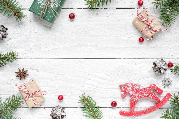 Christmas composition. frame made of fir branches, red berries, retro christmas toy, gift boxes and pine cones on white wooden table. Christmas background. Flat lay. top view with copy space