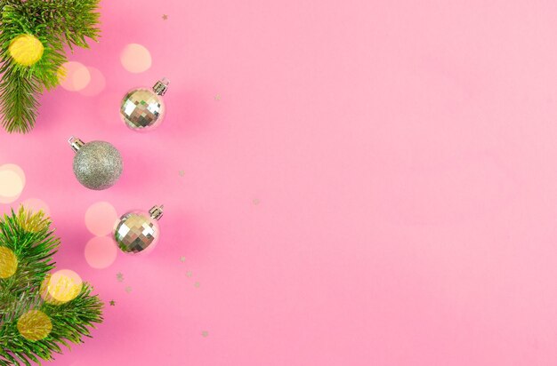 Christmas composition of silver balls confetti and fir branches on a pink background Copy space