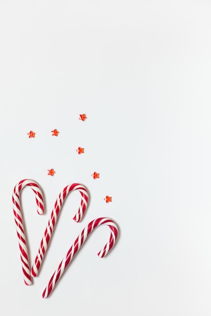 Christmas composition three caramel candy canes, confetti stars on white background with copy space.