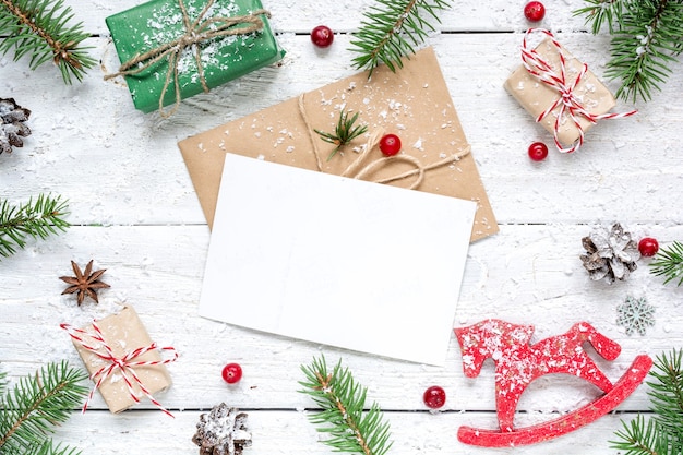 Christmas composition with blank greeting card. fir tree branches, horse toy, gift boxes and cones frame