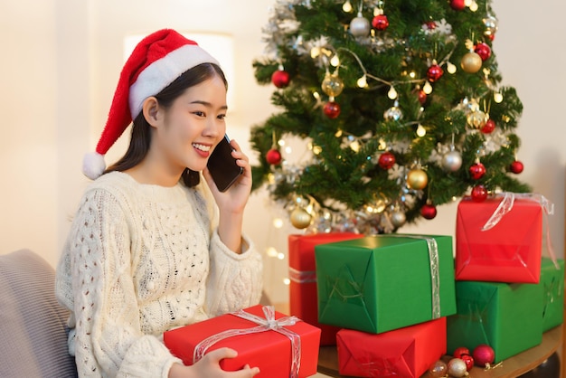 Christmas concept Asian woman sitting in christmas decorated living room and talking on smartphone