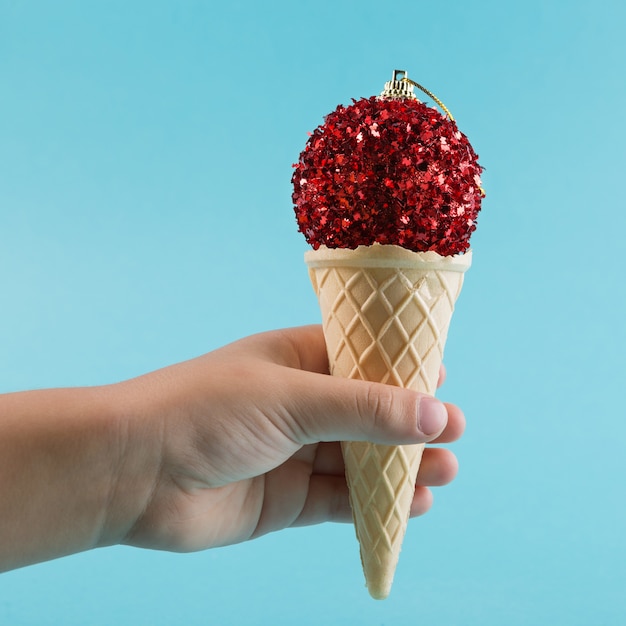 Photo christmas concept, the baby's hand holds a waffle horn from ice cream, a red christmas tree toy