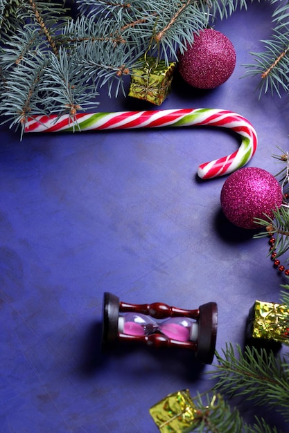 Christmas concept Christmas toys hourglass candy cane Christmas tree branches on a purple background Closeup