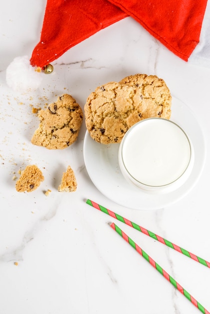 Photo christmas concept, greeting card. milk glass and cookies for santa claus with santa's hat on white marble scene