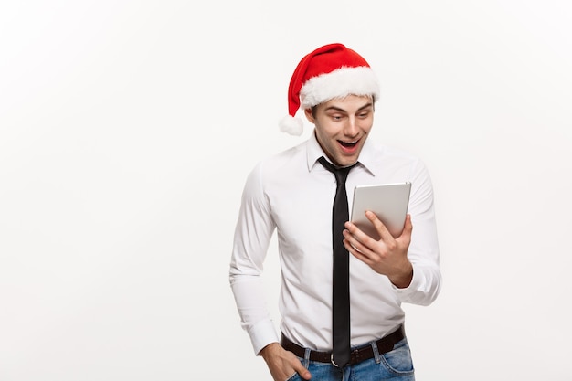 Christmas Concept - Handsome Businessman wear santa hat playing tablet with surprising facial expression.