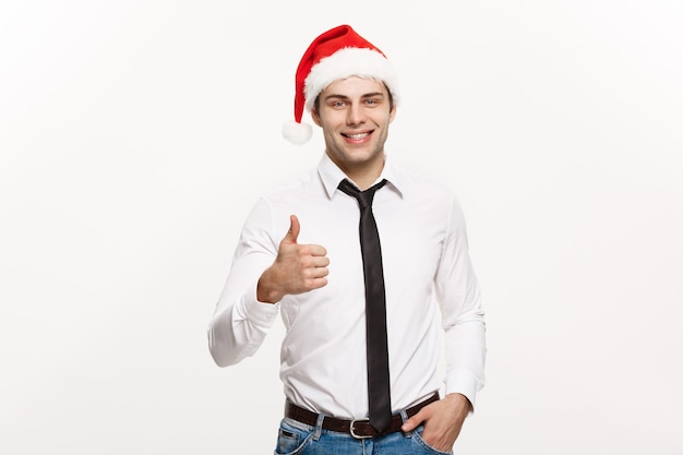 Christmas Concept - Handsome Businessman wear santa hat showing thump up on white isolated wall.