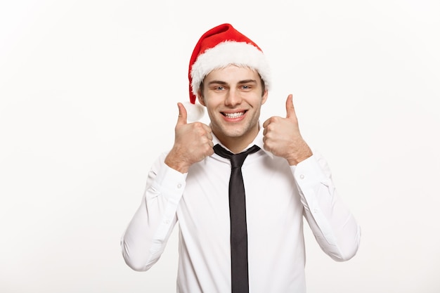 Christmas Concept - Handsome Businessman wear santa hat showing thump up on white isolated wall.