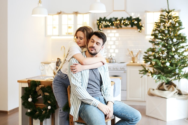 Christmas concept, man and woman in love hug and kiss in the decorated bright kitchen at home