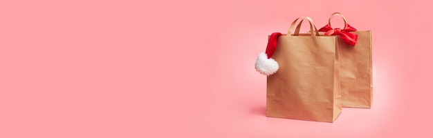 Christmas concept, two paper bags with christmas hat, on pink background, banner, copy space, mock up