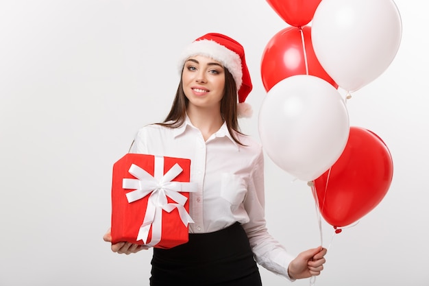 Christmas concept  young happy caucasian business woman with santa hat holding gift box and balloon with copy space on side