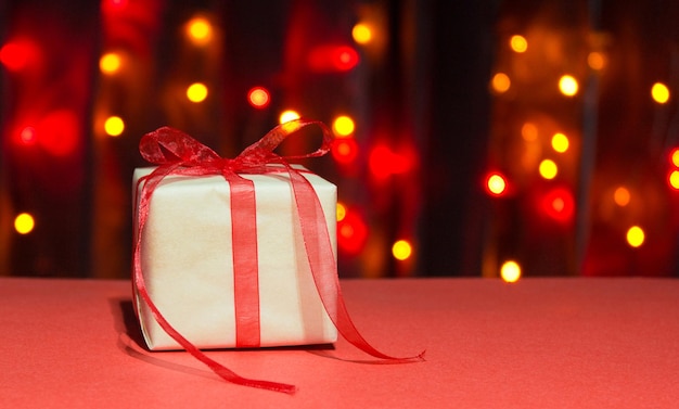 Christmas cube present box with red ribbon and bow on a background of multicolored bokeh. High quality photo