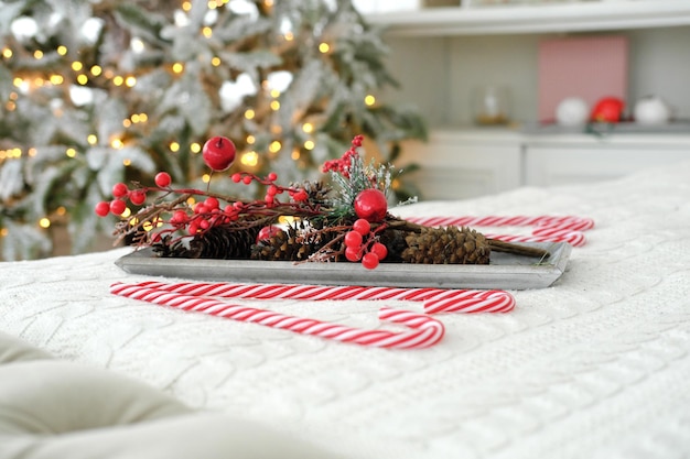 Christmas decor in the form of an artificial branch with red berries and cones on a tray on the bed against the backdrop of Christmas lights