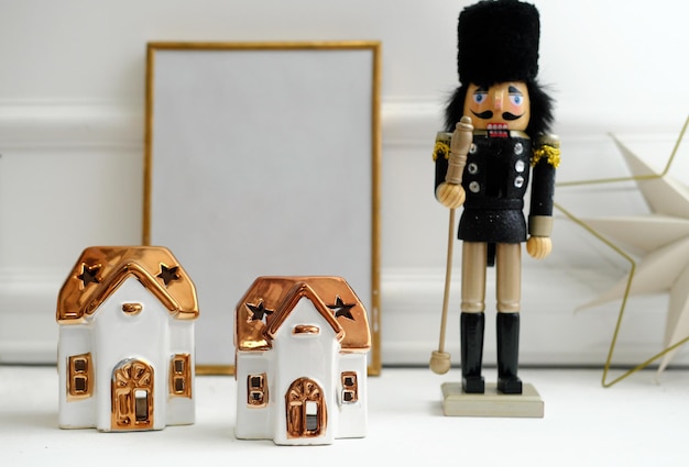 Christmas decor Nutcracker and candles in the form of houses stand on a white shelf An empty frame for text stands on a shelf