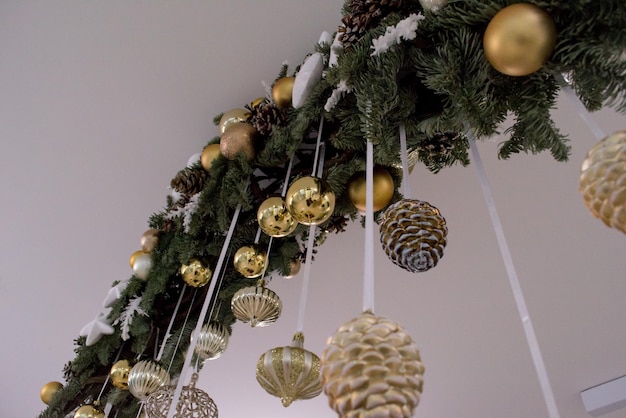 Christmas decoration, fir branch with golden festive balls and fir cones hanging on the ceiling