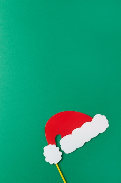 Christmas decoration, red Santas hat on stick on green background with copy space