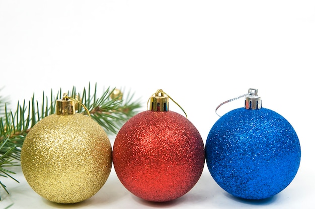 Christmas decoration, three Christmas balls red blue and yellow on a white background close-up and a branch of a fir tree