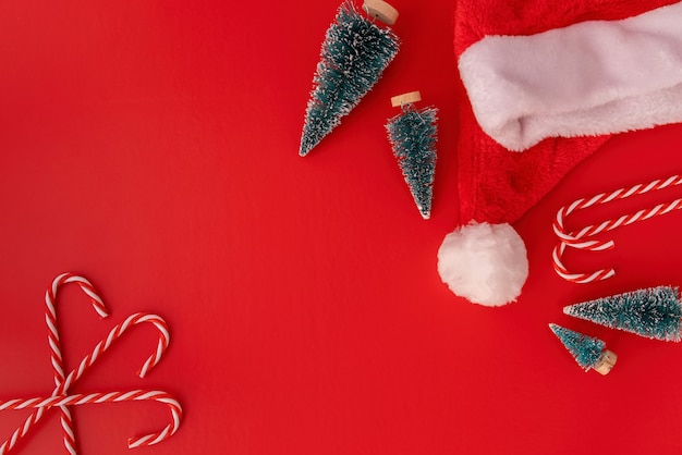 Christmas decorations candy canes, fir trees and sants hat top view on red 