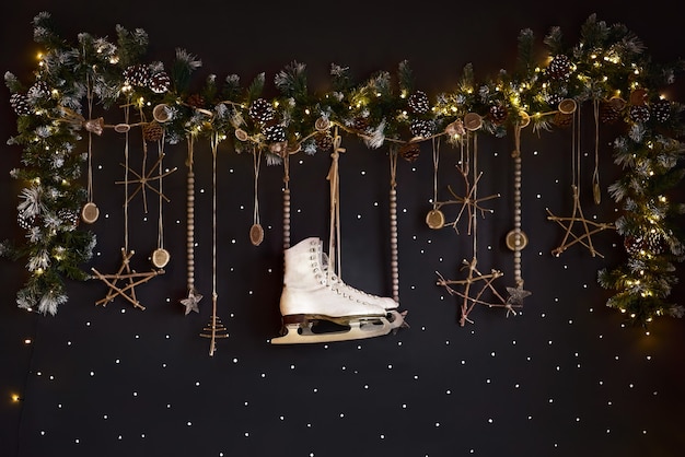 Photo christmas decorations on a dark wall, happy holiday. wall is decorated with a garland with ate tree branches and white skates. expectations of winter.