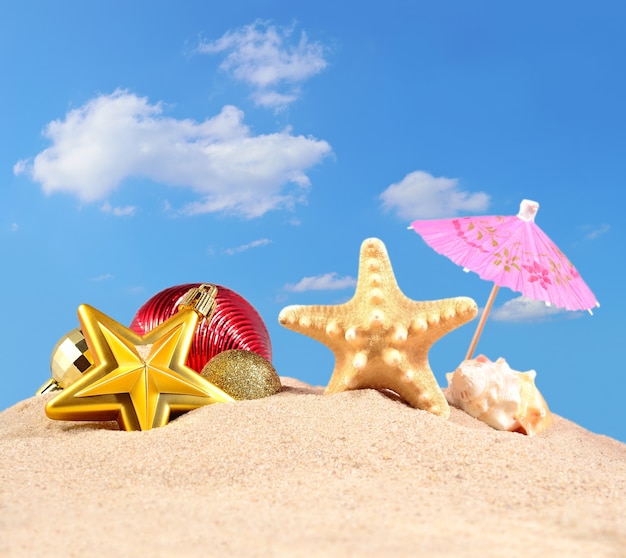 Christmas decorations seashells and starfish on a beach sand against the blue sky