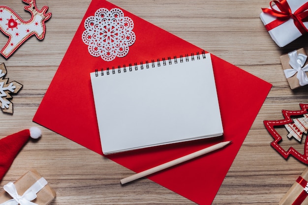 Christmas decorations, toys and gift boxes on wooden table. Blank sketchbook with a pencil to write best wishes.