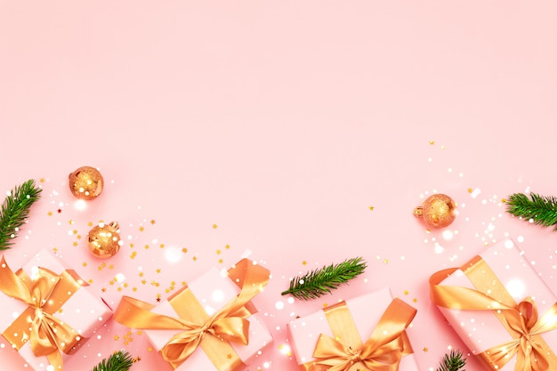 Christmas decorative composition with paper gift box, gold Christmas balls and gold ribbon bow on a pink background