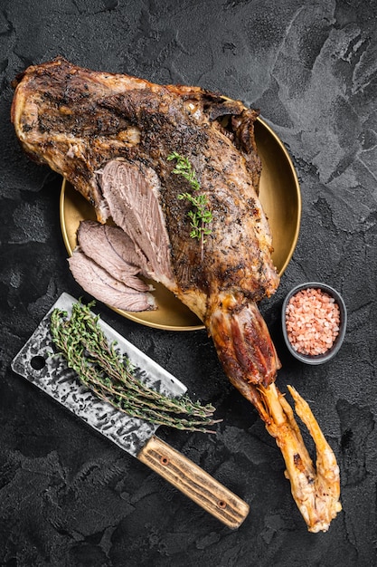 Christmas dish Roast lamb leg meat with spices and thyme on a plate Black background Top view