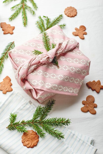 Christmas eco-friendly gift wrap in traditional japanese furoshiki style decorated with fir twigs and gingerbread cookies on fabric