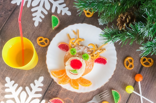 Christmas edible deer of buns and marmalade on a plate on a wooden table next to candy