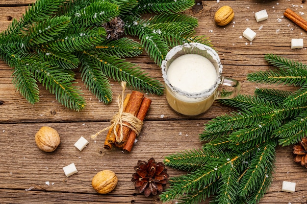 Christmas eggnog liqueur or cola de mono cocktail. Classical winter drink in glass mug, xmas decorations. Evergreen branches, cinnamon, walnuts, sugar.