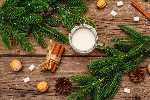 Christmas eggnog liqueur or cola de mono cocktail. Classical winter drink in glass mug, xmas decorations. Evergreen branches, cinnamon, walnuts, sugar.