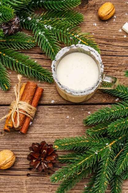 Christmas eggnog liqueur or cola de mono cocktail. Classical winter drink in glass mug, xmas decorations. Evergreen branches, cinnamon, walnuts, sugar.