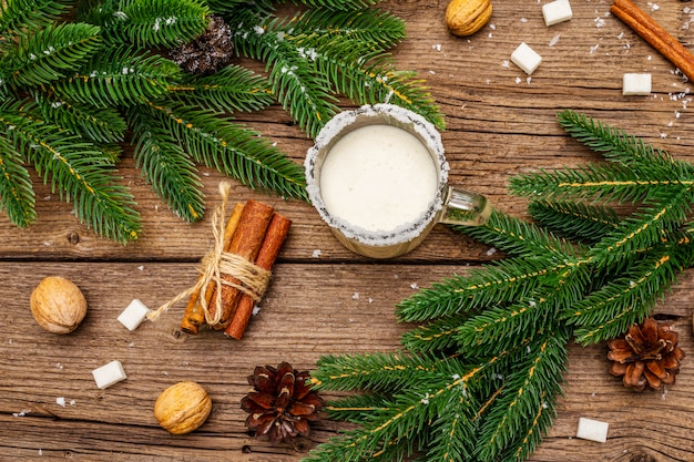 Christmas eggnog liqueur or cola de mono cocktail. Classical winter drink in glass mug, xmas decorations. Evergreen branches, cinnamon, walnuts, sugar.