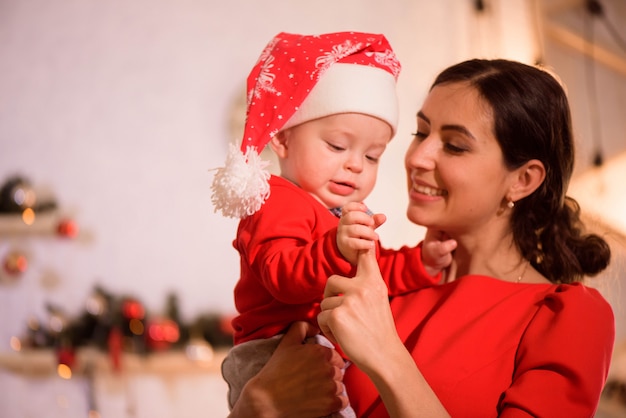 Christmas Eve. family mother and baby in Santa hatplay game at home near the fireplace