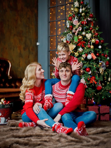 Christmas family portrait in red traditional sweaters in home holiday living room, parents and child with gift box.