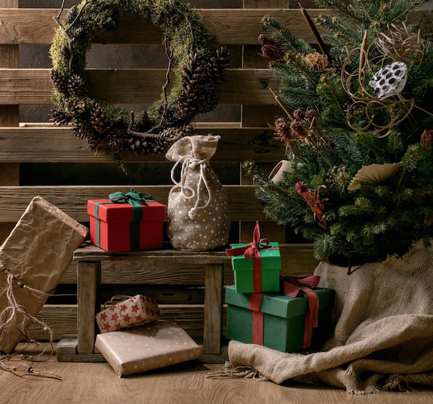 Christmas fashion rustic style interior decor. Craft gift boxes with DIY natural moss wreath and Christmas fir tree with dried flowers. Wooden pallet as background. Trend eco-friendly holidays