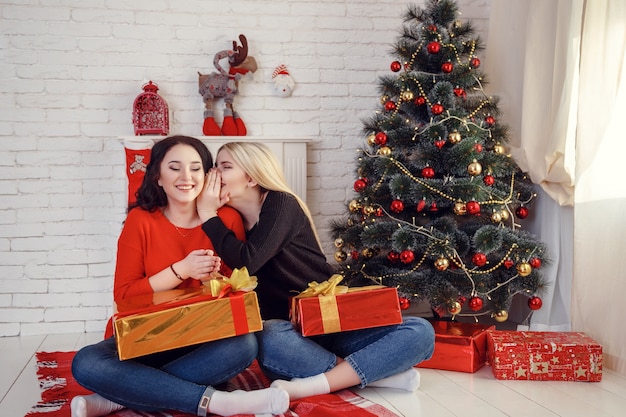 Christmas feeling. After Christmas party. Girls with happy faces near Christmas tree on wooden wall.