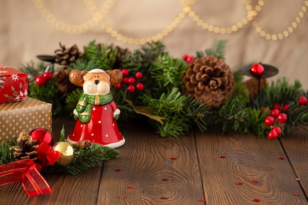 Christmas festive background with a toy reindeer dressed as Santa Claus a Christmas tree decorated with golden lights on a wooden table closeup copy space