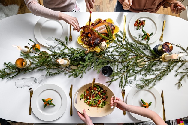 Christmas festive dinner. Delicious traditional holiday meal and hands of people eating them. Decorated table with tasty dishes. Flat Ley. White table