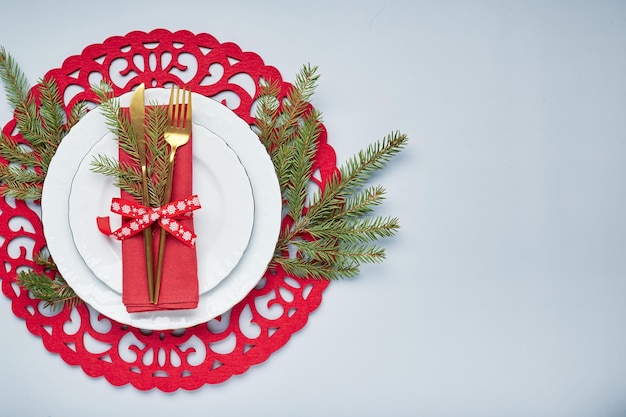 Christmas festive table setting with white plates and gold cutlery red linen napkin fir branches red