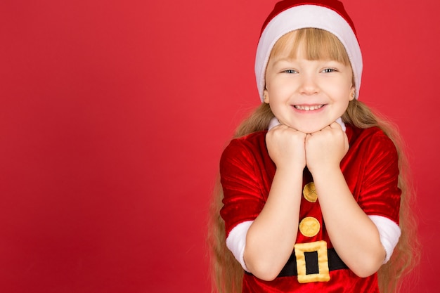 Christmas fever. Horizontal portrait of a little adorable girl in Christmas outfit posing in studio on red