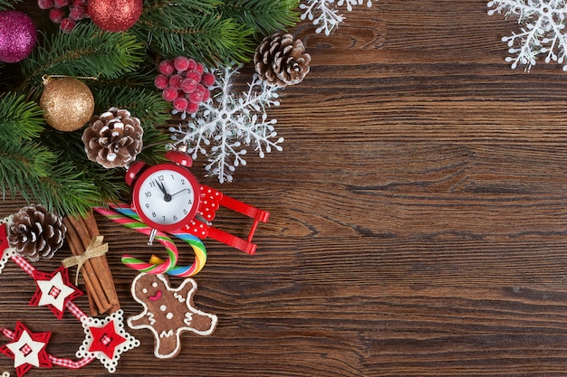 Christmas fir tree with decoration, gingerbread man and red clock on brown wooden background with copy space. Top view, flat lay